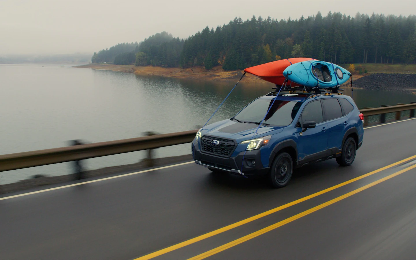 A 2022 Subaru Forester Wilderness on a road by lake with kayaks on roof.