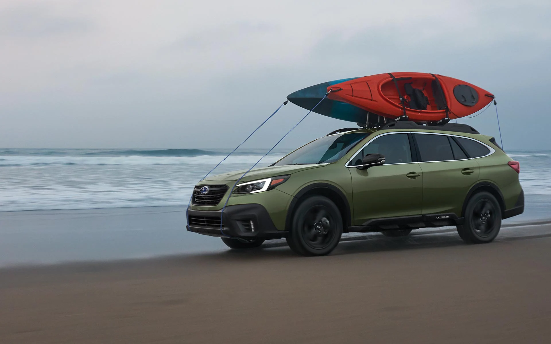 A 2022 Subaru Onyx Edition XT driving on a beach with kayaks mounted to its raised roof rails.